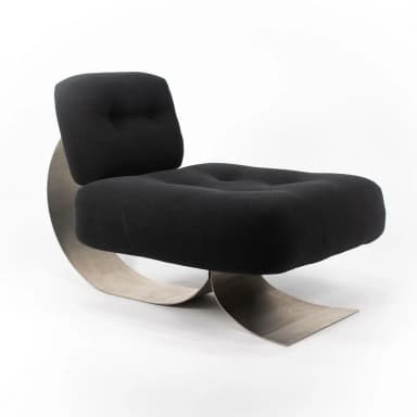 A postmodern lounge chair featuring a distinctive sculptural brushed metal base supporting a plush, black upholstered seat and backrest. The base is formed by a continuous, wide C-shaped metal band that curves elegantly from the floor, up to support the back, and then back down to form the front leg structure. The seat and back are generously padded and upholstered in black fabric, with subtle button tufting on the seat. The backrest is affixed to the metal support with visible hardware, including two black spherical elements. — 3D model