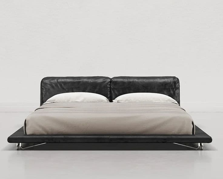 A contemporary low-profile bed frame with a plush, upholstered headboard. The headboard appears to be made of a soft material, possibly leather or a high-quality fabric, and is divided into two distinct sections. The frame itself is sleek and minimalistic, with a wide platform base. The bed is dressed with white pillows and a light-colored duvet. The base of the bed is supported by slim, metallic legs that are partially visible. — 3D model