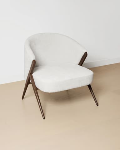 A modern armchair with a rounded back and seat, upholstered in a textured off-white fabric. The frame and legs are made of dark wood, featuring an angular, open design that supports the upholstered shell. — 3D model