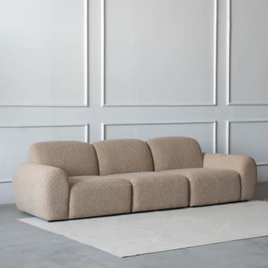 A contemporary three-seater modular sofa featuring soft, rounded forms and upholstered in a light beige, textured fabric. The sofa comprises three distinct sections, each contributing to a cohesive, low-profile design. — 3D model