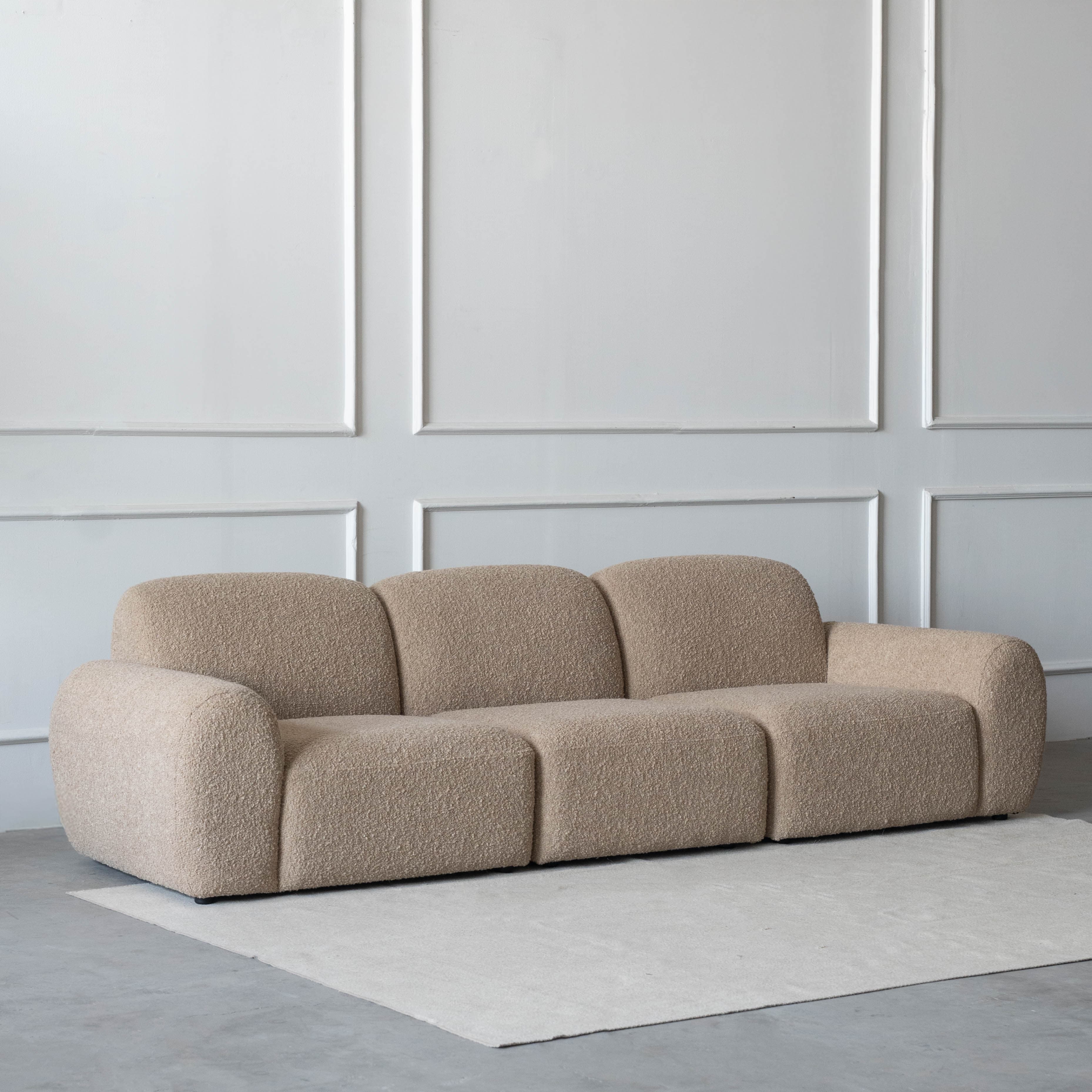A contemporary three-seater modular sofa featuring soft, rounded forms and upholstered in a light beige, textured fabric. The sofa comprises three distinct sections, each contributing to a cohesive, low-profile design. — 3D model