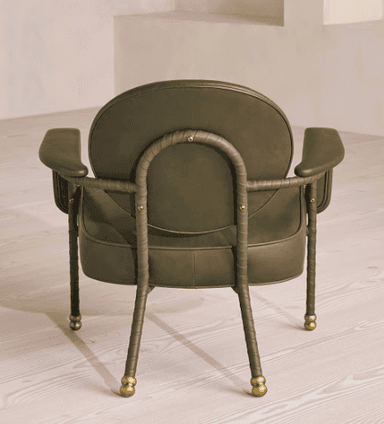 A contemporary armchair with a rounded backrest and armrests, upholstered in a muted olive-green material. The frame appears to be made of metal with a dark finish, and the legs are slender with decorative brass caps. — 3D model