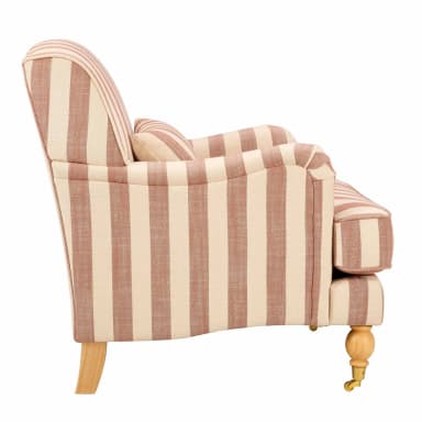 A single-seater armchair with a cushioned seat, backrest, and armrests, upholstered in a striped fabric. It features a decorative bolster cushion and stands on four turned wooden legs with brass casters on the front two. — 3D model