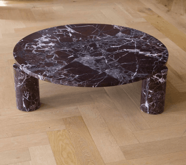 A circular coffee table with a dark marble top and four cylindrical legs made of the same material. The legs are positioned to support the tabletop, with two visible from the front in this view. The marble exhibits a pattern of white veining against a deep reddish-brown background. — 3D model