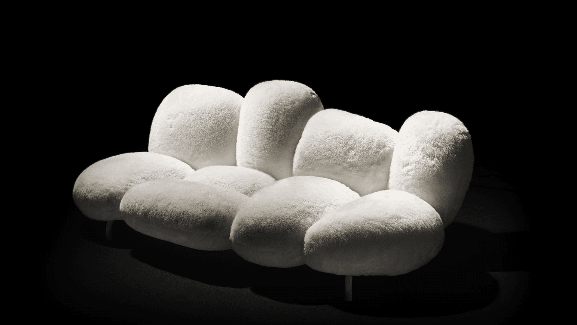 A contemporary three-seater sofa composed of multiple organically shaped, rounded cushions upholstered in a soft, light-colored bouclé fabric. The design mimics large pebbles or clouds, featuring a low profile supported by subtle, minimalist legs. — 3D model