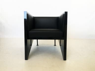 A pair of modern armchairs with a distinctive geometric design, featuring angular dark-stained wood or laminate frames and black leather seat and back cushions. The chairs present a minimalist and architectural aesthetic. — 3D model