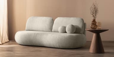 A modern, low-profile sofa with a rounded, organic form. The sofa is upholstered in a textured, boucle-like fabric. It features a continuous seat cushion that curves upwards at the sides, and two separate back cushions. Two spherical decorative pillows are placed on the left side of the sofa. — 3D model