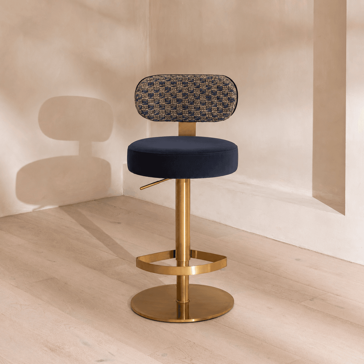 A modern adjustable height bar stool featuring a dark blue velvet upholstered seat and a patterned woven fabric backrest. It is supported by a polished golden metal column, a circular footrest, and a wide circular base. — 3D model