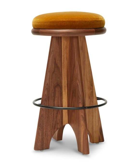 A modern bar stool featuring a round, thickly padded seat upholstered in a rich golden-yellow velvet or plush fabric, resting on a substantial, sculptural walnut wood base. The base is composed of several broad, tapered planks that flare outwards towards the bottom, creating a robust and stable foundation. A circular black metal ring serves as a footrest, integrated into the lower portion of the wooden base. — 3D model