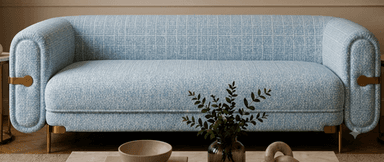 A contemporary three-seater sofa upholstered in a light blue textured fabric, featuring distinctively rounded armrests and backrest. The sofa is supported by slender, tapered brass-finished metal legs and includes decorative horizontal brass bars integrated into the outer sides of the armrests, adding a touch of metallic contrast to the soft upholstery. — 3D model