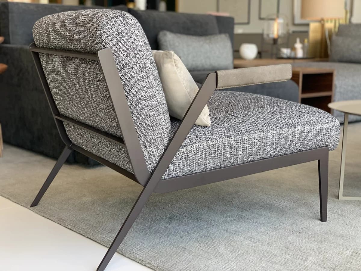 A modern lounge chair featuring a dark grey open metal frame, upholstered in a speckled grey fabric. It has wide, comfortable cushions for the seat and back, and light grey leather or faux leather armrest pads. A small, light-colored decorative pillow rests on the seat. — 3D model