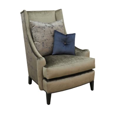 A fully upholstered wingback armchair, featuring a high back with subtly flared wings and rolled arms. It is covered in a textured, greenish-beige fabric, likely velvet or chenille. Decorative nailhead trim runs along the armrests and the bottom edge of the chair's frame. The chair rests on short, dark, tapered wooden legs. It is adorned with two accent pillows: one large rectangular pillow with a grey and beige abstract pattern, and a smaller solid navy blue square pillow with a central button tuft. — 3D model