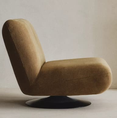 A modern armchair with a low profile and a distinctive upholstered shell. It features a single pedestal base, likely for swivel functionality. The upholstery appears to be a textured fabric with a woven appearance. The design emphasizes rounded forms and a comfortable, enveloping silhouette. — 3D model