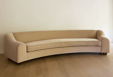 A modern curved sofa featuring a beige upholstered fabric, low profile, and simple block feet. The design includes fixed back and seat cushions, with gently rolled arms that flow into the curved backrest. — 3D model