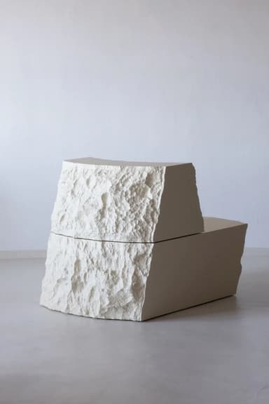 A sculptural lounge chair composed of two block-like pieces, resembling carved stone, in an off-white or beige color. The pieces have smooth top surfaces and rough, chiseled sides, with one serving as the seat and the other as a backrest. — 3D model