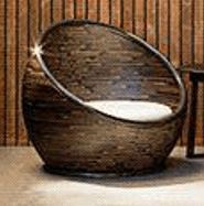 A contemporary globe-shaped lounge chair, featuring a deeply curved body constructed from dark brown woven synthetic rattan. The spherical form is supported by a subtle metal frame, visible as a trim around the edges and base. A circular, white fabric cushion provides seating within the chair's recessed interior. The design suggests a cozy, encompassing seating experience, suitable for modern or outdoor settings. — 3D model