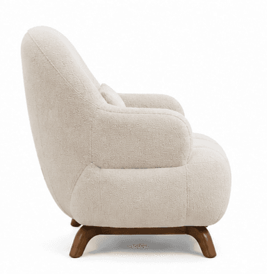 An upholstered armchair featuring a plush, rounded silhouette. The chair is covered in a textured cream-colored boucle fabric. It has integrated, softly curved arms and a continuous backrest. The seat base includes subtle vertical channel tufting. The chair rests on short, splayed dark wood legs. A matching rectangular lumbar pillow is included. — 3D model