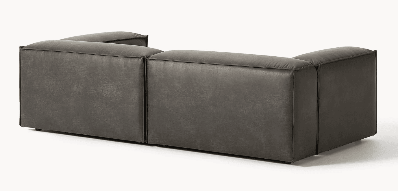 A dark grey modular sectional sofa, upholstered in distressed faux leather, featuring a low profile and rounded, plush cushions, seen from the rear and side. — 3D model