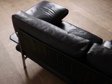 A modern three-seater sofa upholstered in black leather, featuring a minimalist design with a visible slim metal frame. It has three individual seat cushions, three back cushions, and detached, cushioned armrests, all in matching black leather. The sofa stands on slender metal legs, contributing to its sleek, elevated profile. — 3D model