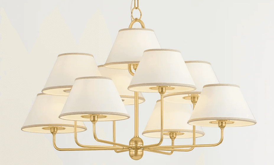 A contemporary or transitional chandelier featuring a satin brass finish and nine individual tapered fabric shades. The fixture is suspended by a chain and has multiple arms radiating outwards from a central hub, each supporting a light source covered by a cream-colored shade with subtle trim. — 3D model