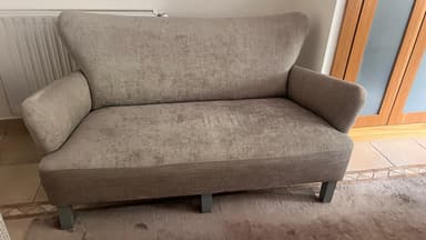 A two-seater sofa with a curved back and armrests. The upholstery appears to be a textured fabric with a subtle distressed pattern. The legs are angular and support the sofa from underneath. — 3D model