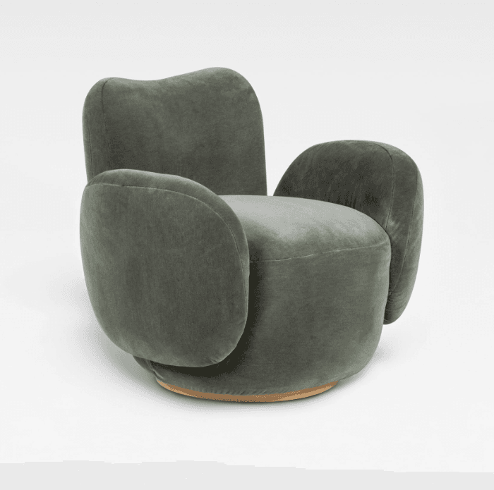 An upholstered lounge chair featuring an organic, rounded silhouette, covered in a soft, sage-green velvet-like fabric. The chair has broad, sculptural armrests that curve outwards from the seat, and a gently reclined backrest. It sits on a low, cylindrical wooden plinth base, giving it a contemporary and inviting appearance. — 3D model