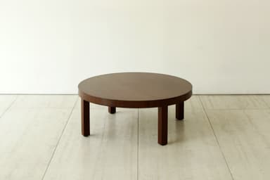 A minimalist round coffee table crafted from dark wood, featuring a thick circular top supported by four sturdy, rectangular legs. The design is simple and functional. — 3D model