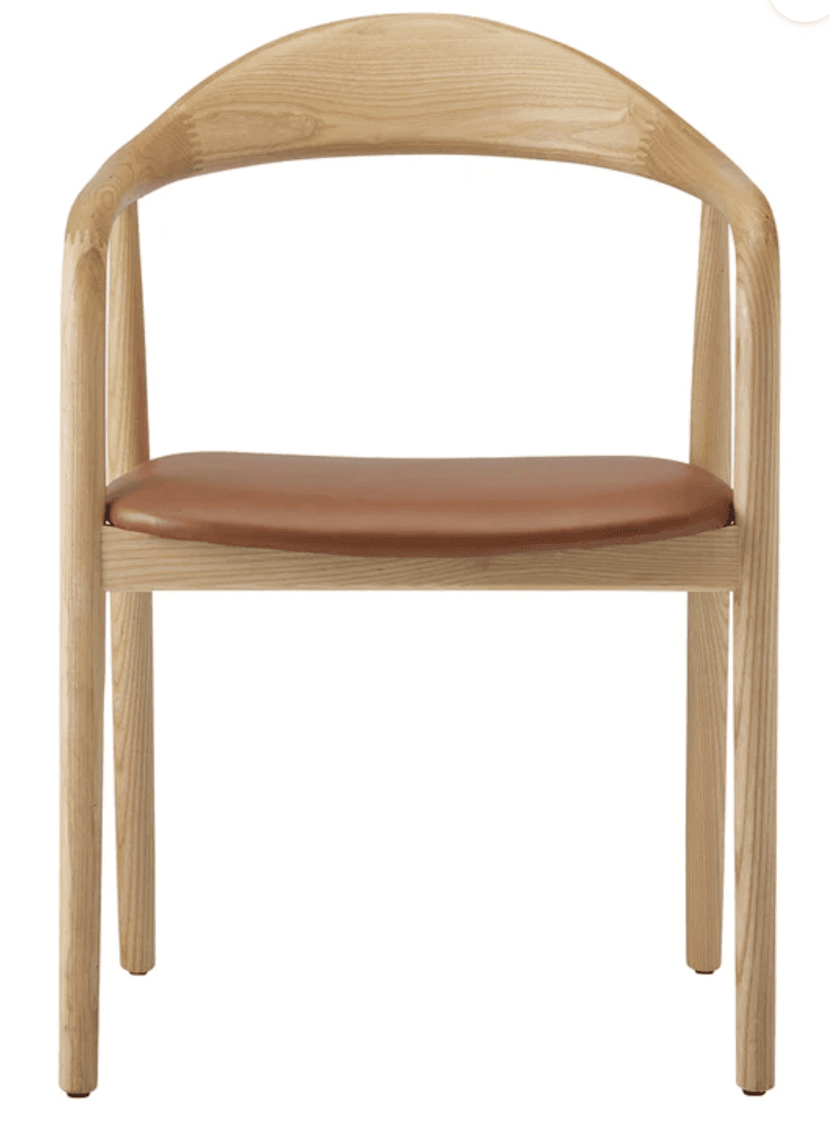 A Scandinavian modern armchair constructed from light-colored ash wood with a subtly visible grain. It features a continuous, gently curved element that forms both the backrest and the armrests, creating a fluid silhouette. The seat is a flat, padded cushion upholstered in a cognac-colored leather or faux leather. The frame is supported by four round, slightly tapered legs, connected by simple stretchers beneath the seat. — 3D model