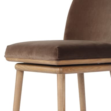 A bar stool with a wooden base and a upholstered seat and backrest. The stool has a swivel mechanism. The wooden legs are angled outwards, and there are crossbars for stability. The seat and backrest are covered in a textured fabric, likely velvet, in a brown hue. — 3D model