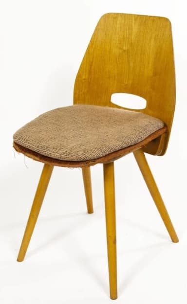 A vintage mid-century modern side chair featuring a bent plywood frame with a light wood veneer finish. It has a distinctive curved backrest with an oval cutout serving as a handle. The seat is upholstered in a textured, light brown fabric, and the chair stands on four splayed, tapered wooden legs. — 3D model
