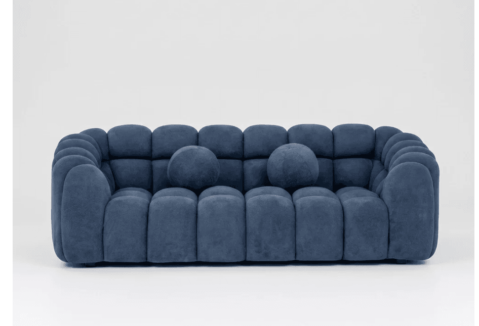 A modern three-seater sofa characterized by its sculptural, rounded, segmented design, upholstered in a deep blue velvet-like fabric and accompanied by two matching spherical toss pillows. — 3D model