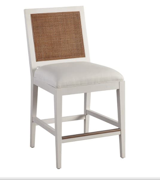 A counter-height bar stool with a square seat and a rectangular back. The frame is constructed from wood, painted white. The seat is upholstered in a light-colored, textured fabric. The backrest features a cane-woven insert framed by the white wood. The legs are straight, and a horizontal wooden support with a thin metal accent spans between the front and rear legs on each side. — 3D model
