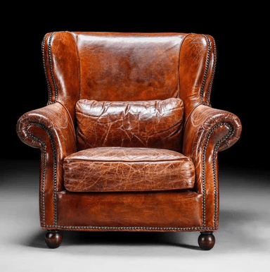 A traditional wingback armchair upholstered in rich, distressed brown leather, featuring prominent wingback sides, rolled arms, and extensive nailhead trim. It includes a loose seat cushion and a loose back cushion, supported by dark turned wooden bun feet. — 3D model