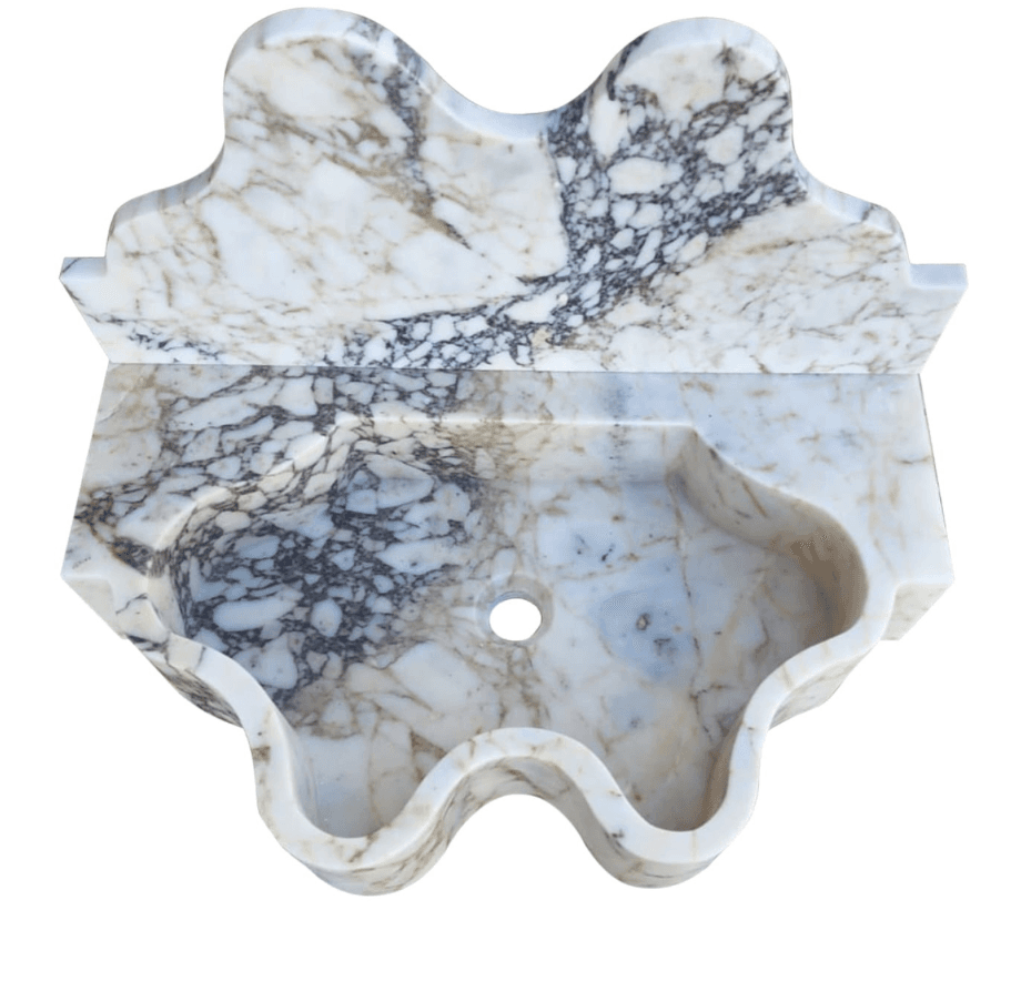 A wall-mounted sink carved from a single piece of marble. It features an intricately shaped basin with a central drain hole and a decorative, scalloped front edge. The back of the sink extends upwards to form a splashback, also with decorative shaping. The marble exhibits a complex veining pattern in shades of white, cream, brown, and dark gray. — 3D model