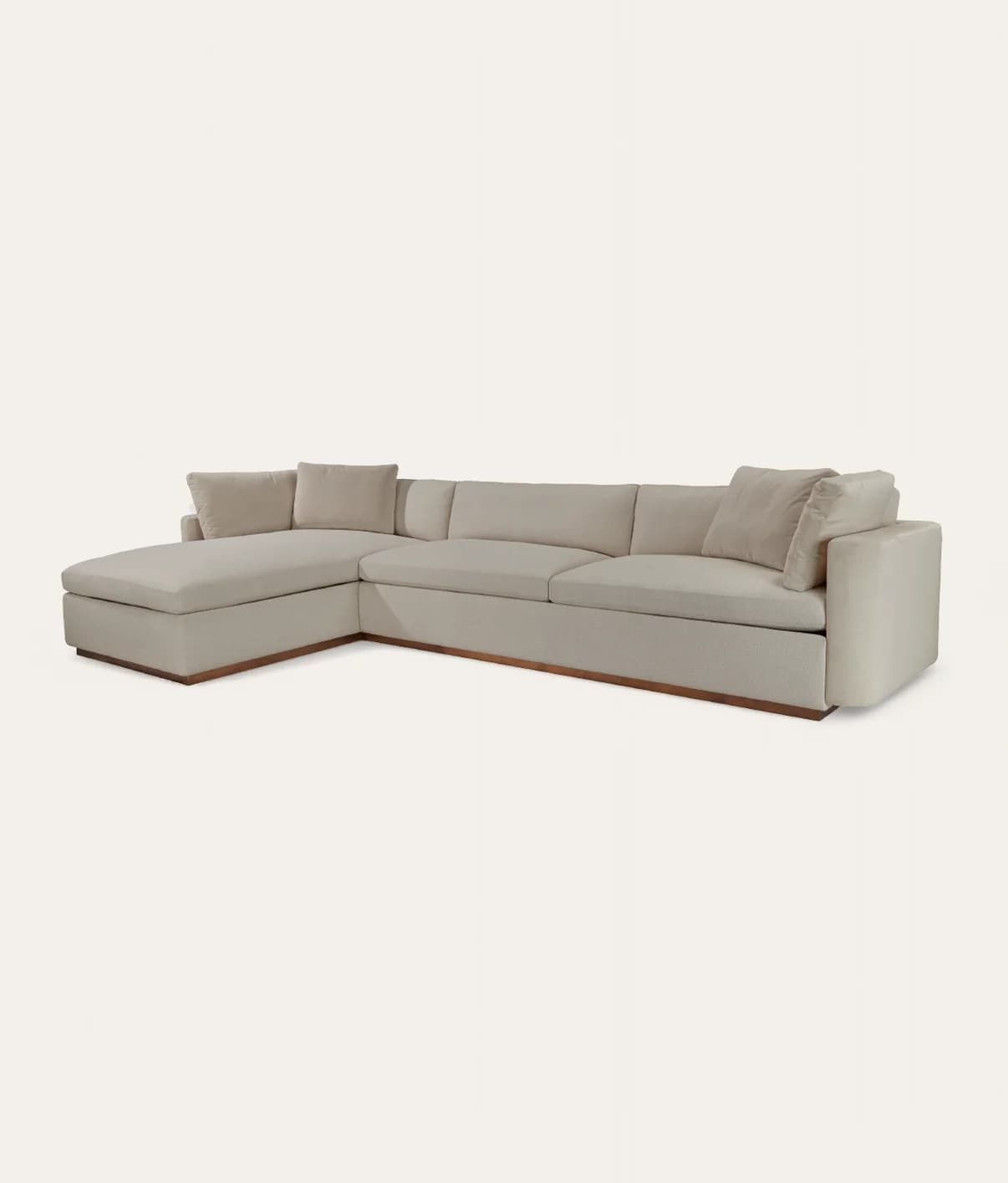 A large L-shaped sectional sofa featuring a neutral-toned fabric upholstery. It includes multiple seat and back cushions, along with loose throw pillows. A prominent left-hand facing chaise extension provides ample lounging space. The sofa is supported by a recessed wooden plinth base, giving it a floating appearance. Wide, upholstered arms contribute to its contemporary aesthetic. — 3D model