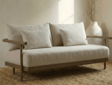 A contemporary two-seater sofa featuring a minimalist design with a visible wooden frame and light beige fabric upholstery. It includes two seat cushions, two back cushions, and two small throw pillows. The armrests are simple, cylindrical wooden bars extending from the frame. — 3D model