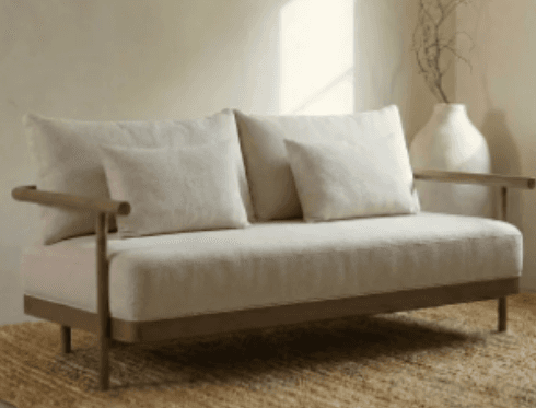 A contemporary two-seater sofa featuring a minimalist design with a visible wooden frame and light beige fabric upholstery. It includes two seat cushions, two back cushions, and two small throw pillows. The armrests are simple, cylindrical wooden bars extending from the frame. — 3D model