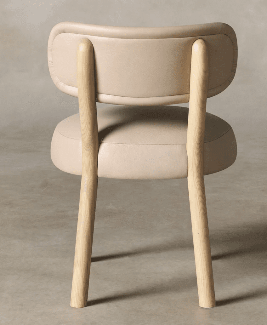 A contemporary armless dining chair featuring a light-toned natural wood frame and plush, rounded cushioning upholstered in a neutral beige or cream material. The design is minimalist, emphasizing comfort and modern aesthetics, shown from the rear. — 3D model