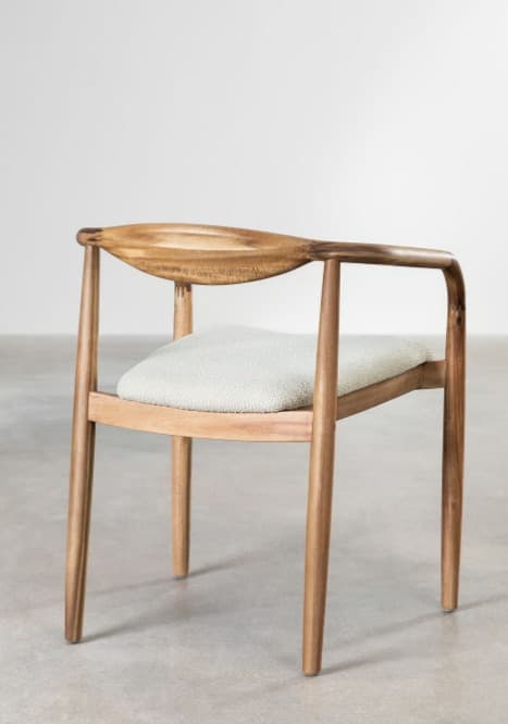 A light-toned wooden armchair featuring a distinctive curved, carved backrest that extends seamlessly into integrated armrests. The chair has an upholstered seat cushion in a light grey fabric, supported by a wooden frame with tapered legs. Its design exhibits clean lines and organic forms, characteristic of Scandinavian or mid-century modern aesthetics. — 3D model