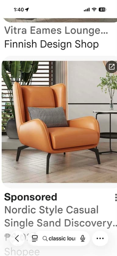 A contemporary armchair with a high back and winged sides, upholstered in tan-colored leather. It features a small, checkered throw pillow placed on the seat. The armchair is supported by four slender, black metal legs with an angular design. — 3D model