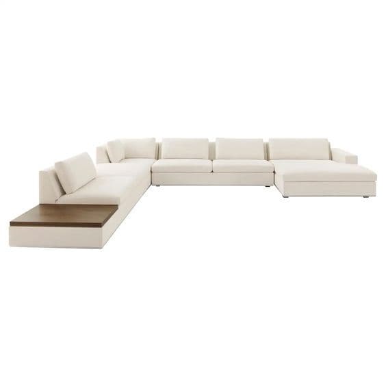 A contemporary, large modular sectional sofa upholstered in a light-colored fabric, featuring a deep chaise lounge and an integrated dark wood side table on one end. — 3D model