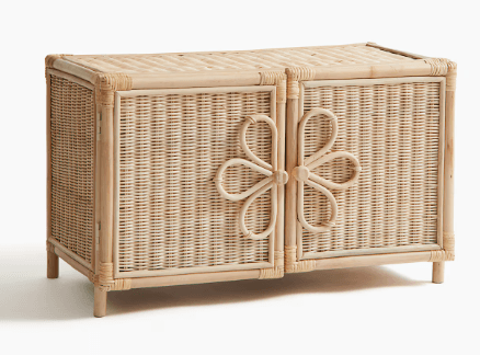 A small, rectangular accent cabinet constructed from woven natural rattan, featuring two front-opening doors. Each door is adorned with a stylized floral or bow-like motif made from bent rattan, which also functions as a handle. The cabinet stands on four short, rounded legs, and the top and side panels are also woven. — 3D model