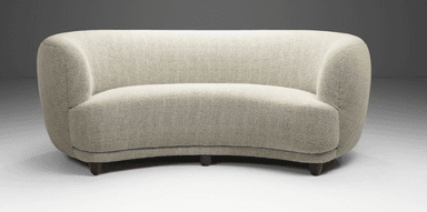 A curved, fully upholstered sofa featuring a serpentine form, rounded back and integrated armrests, and short, tapered wooden legs. It is covered in a light-colored, textured woven fabric. — 3D model