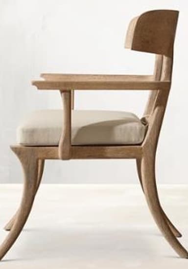 A sturdy wooden dining chair with a light brown upholstered seat and a distinctive curved backrest. The frame is made of a medium-toned wood, featuring gently curved and tapered legs. The backrest is a solid, broad piece of wood, supported by two vertical stiles, with integrated armrests extending from these supports. — 3D model