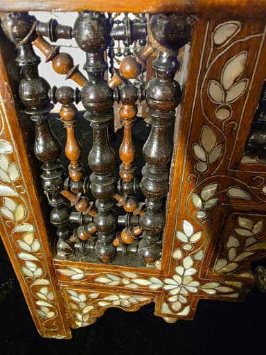 A highly ornate accent chair featuring intricate marquetry and inlay work. The chair has a tall, elaborately carved back with floral motifs and geometric patterns. The seat is upholstered in a light-colored fabric with a floral pattern. The base of the chair, including the legs and the area beneath the seat, is constructed from dark wood and heavily decorated with mother-of-pearl inlay, creating floral and geometric designs. The legs have an arched structure. The overall construction suggests a piece of antique or artisan craftsmanship. — 3D model