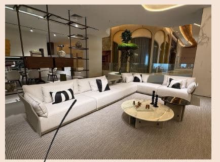 An L-shaped sectional sofa featuring a modern, minimalist design. It is upholstered in a light-colored, textured fabric, likely an off-white or light beige. The sofa comprises multiple modular units forming a right-hand facing L-configuration, with wide, square armrests and backrests. It includes several loose seat cushions and back cushions, along with additional throw pillows, some of which feature a contrasting black and white geometric pattern. — 3D model
