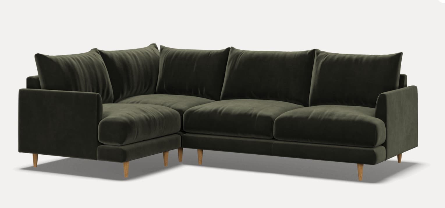 An L-shaped sectional sofa upholstered in dark olive green velvet, featuring a contemporary design with clean lines. It includes multiple plush seat and back cushions, wide track arms, and stands on small, splayed light-colored wooden legs. The modular design suggests flexibility in arrangement. — 3D model