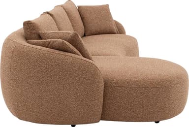 A modern, curved sectional sofa upholstered in a textured, light brown or tan boucle-style fabric. The sofa features a low-profile design with an integrated chaise lounge section on one side, offering ample seating and lounging space. Its backrest and armrests are gently rounded, providing a soft, organic aesthetic. Several loose back cushions are provided for comfort. — 3D model