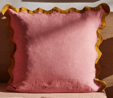 A square-shaped cushion with a pink fabric cover and a decorative mustard yellow ruffled edge. The cushion appears soft and filled, suitable for decorative or comfort purposes. — 3D model