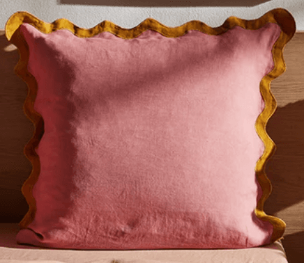 A square-shaped cushion with a pink fabric cover and a decorative mustard yellow ruffled edge. The cushion appears soft and filled, suitable for decorative or comfort purposes. — 3D model